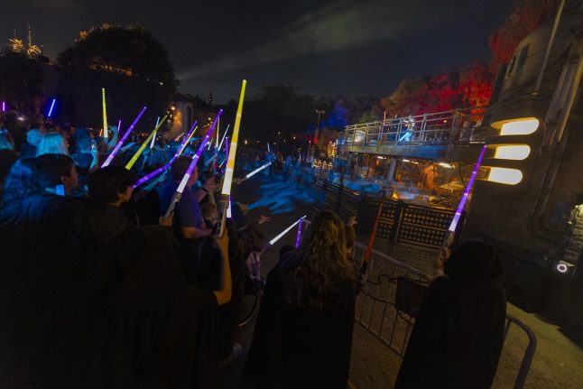 A crowd holds lightsabers up to the sky at night