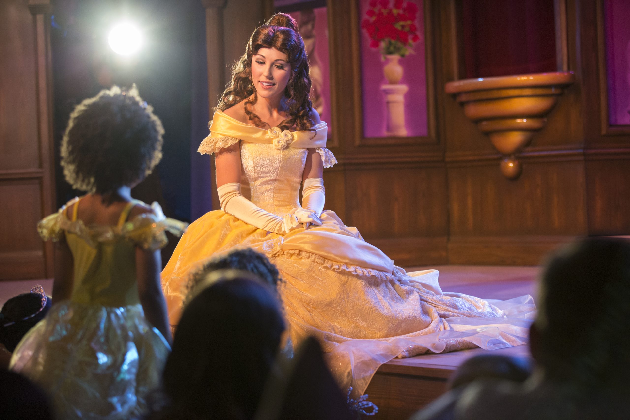 A young child dressed as Tiana talks to Princess Bell while other children look on. 